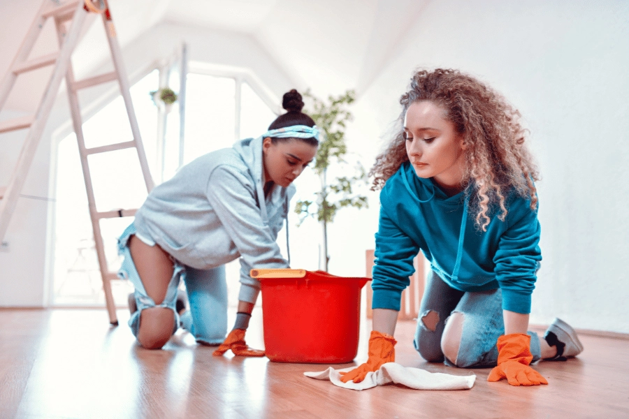 girl roommates cleaning the room together and scrubbing the floor 